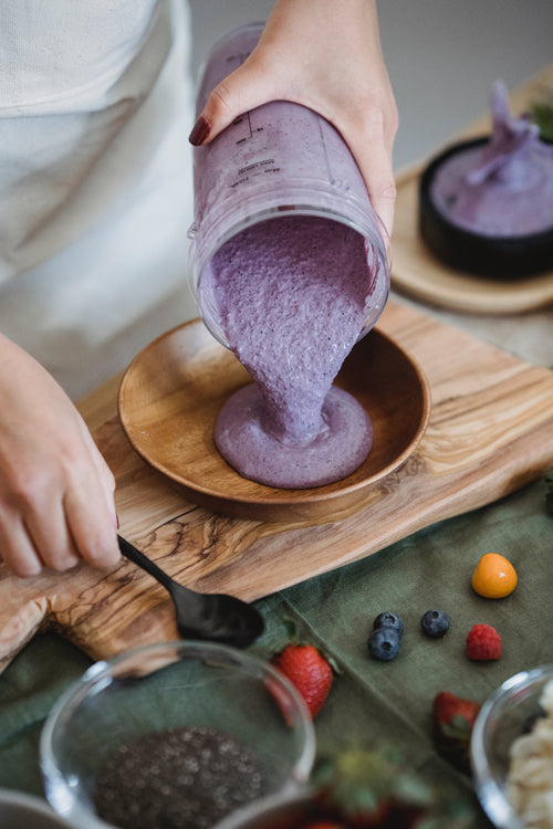 Person pouring immune boosting blueberry smoothie into wooden bowl