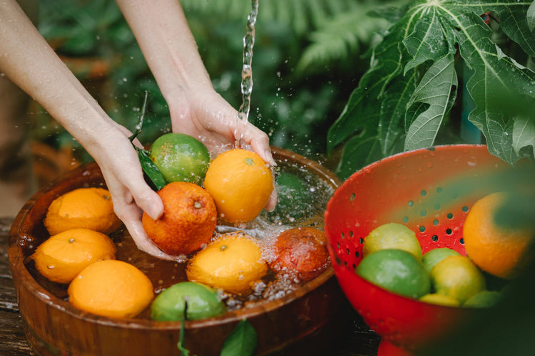 Person washing fruits containing Vitamin C, including oranges and limes