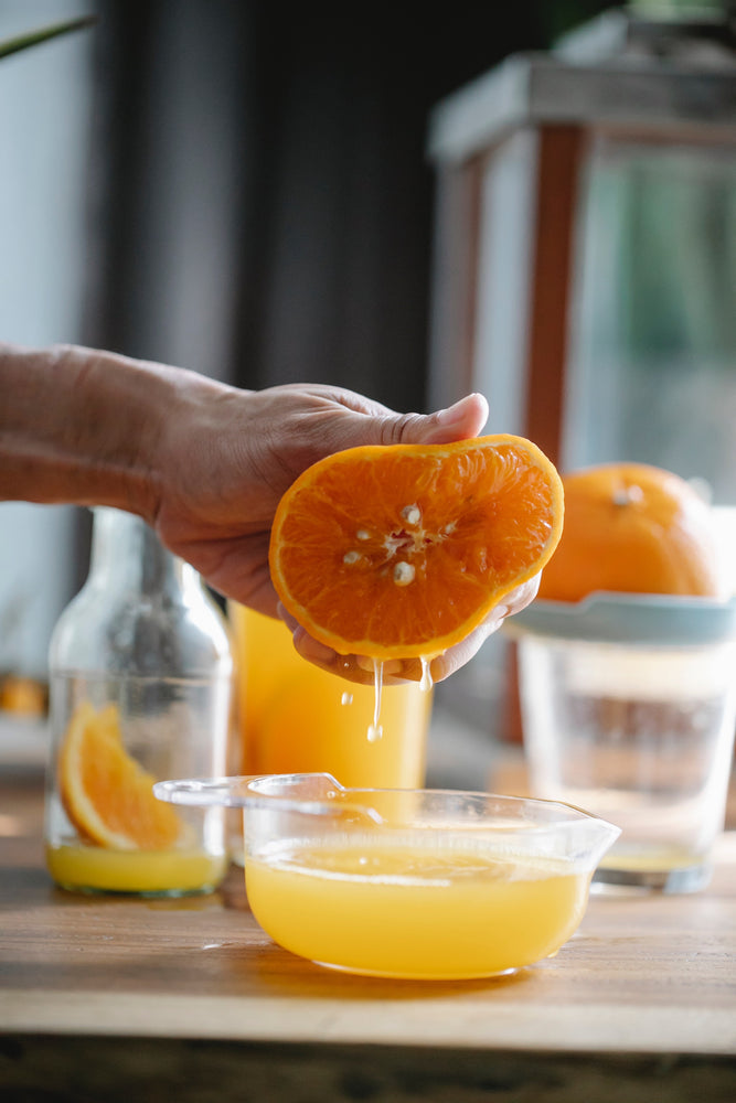 A person juicing an orange into a cup, making a Vitamin C packed orange juice